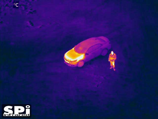 FLIR M1D surveillance camera image of a man by a car in infrared